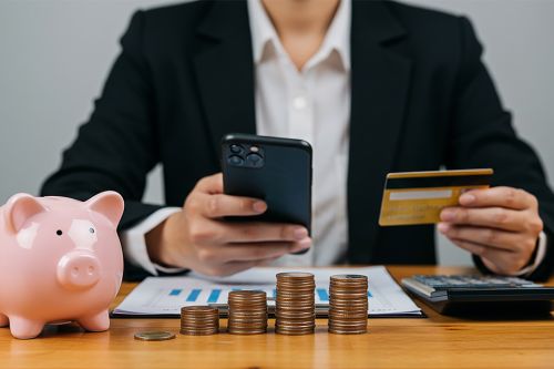 Foto: Mann mit Smartphone, Bankomatkarte, Sparschwein und Münzen